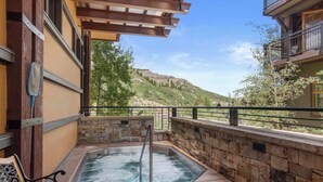Un jacuzzi con pared de piedra y banco de madera, con vistas a un paisaje montañoso.