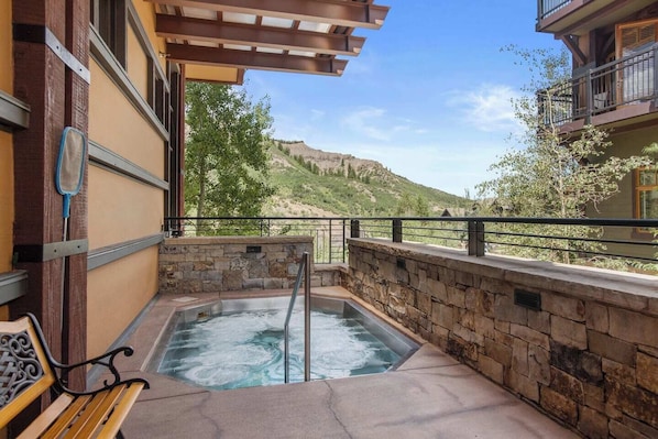 Un jacuzzi con pared de piedra y banco de madera, con vistas a un paisaje montañoso.