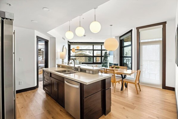 Une cuisine moderne dotée d’un îlot central, d’appareils électroménagers en acier inoxydable et de luminaires suspendus.