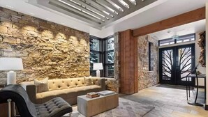 Una sala de estar moderna con una pared de piedra, un sofá color beige, un sillón negro y una mesa de centro.
