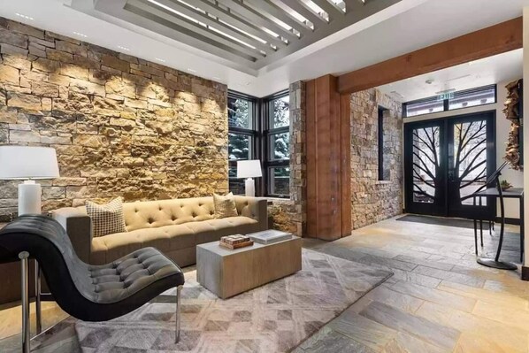 A modern living room with a stone wall, a beige sofa, a black armchair, and a coffee table.