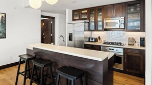Una cocina moderna con una isla central, electrodomésticos de acero inoxidable, armarios de madera oscura e iluminación colgante.