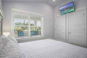 A bedroom with a large bed, a TV mounted above a wardrobe, and a window with blinds.