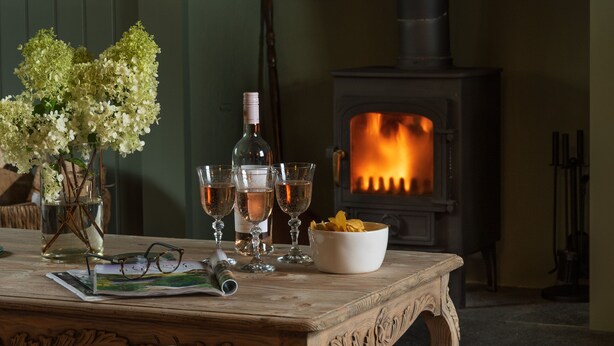 Une pièce chaleureuse avec une cheminée, une table avec des boissons et un vase rempli de fleurs.