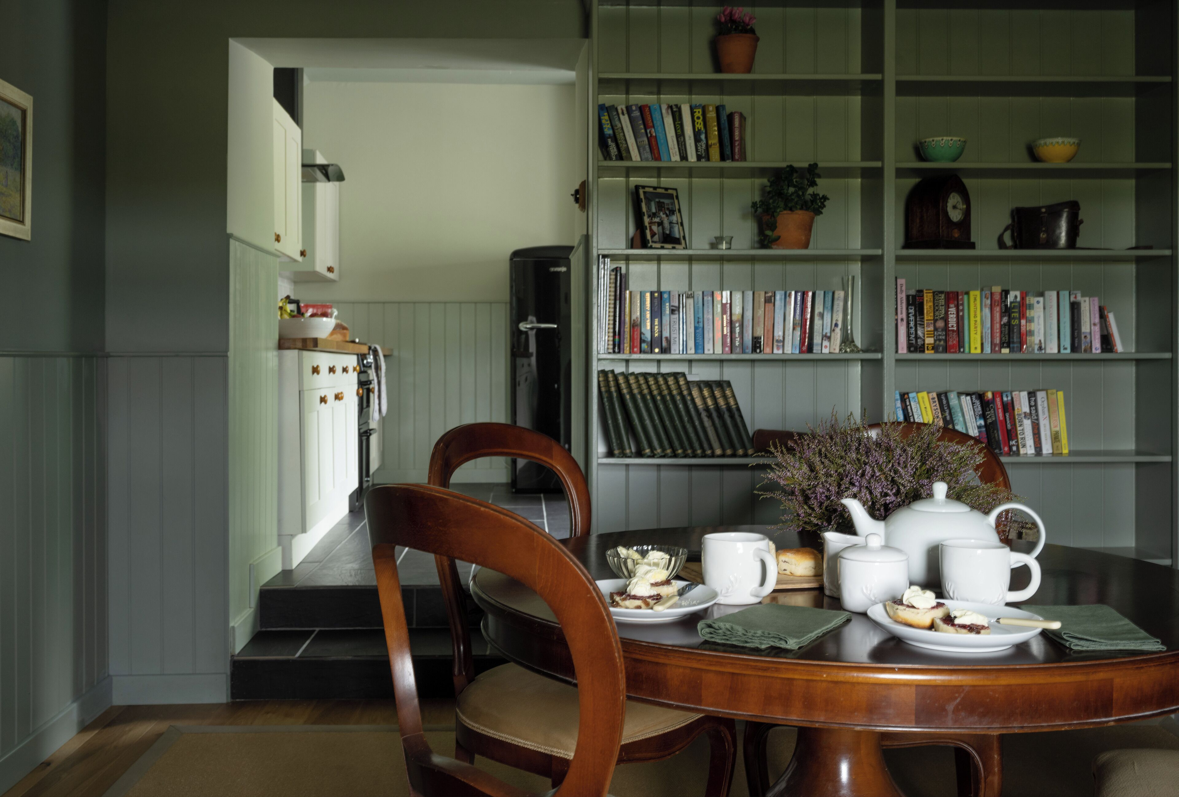 Un comedor con una mesa de madera dispuesta para el té, rodeado de estanterías llenas de libros y objetos decorativos.