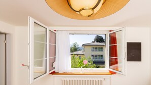 A bedroom with a large window, a radiator below, and a ceiling light fixture. - Villa Maria (Lucerne)