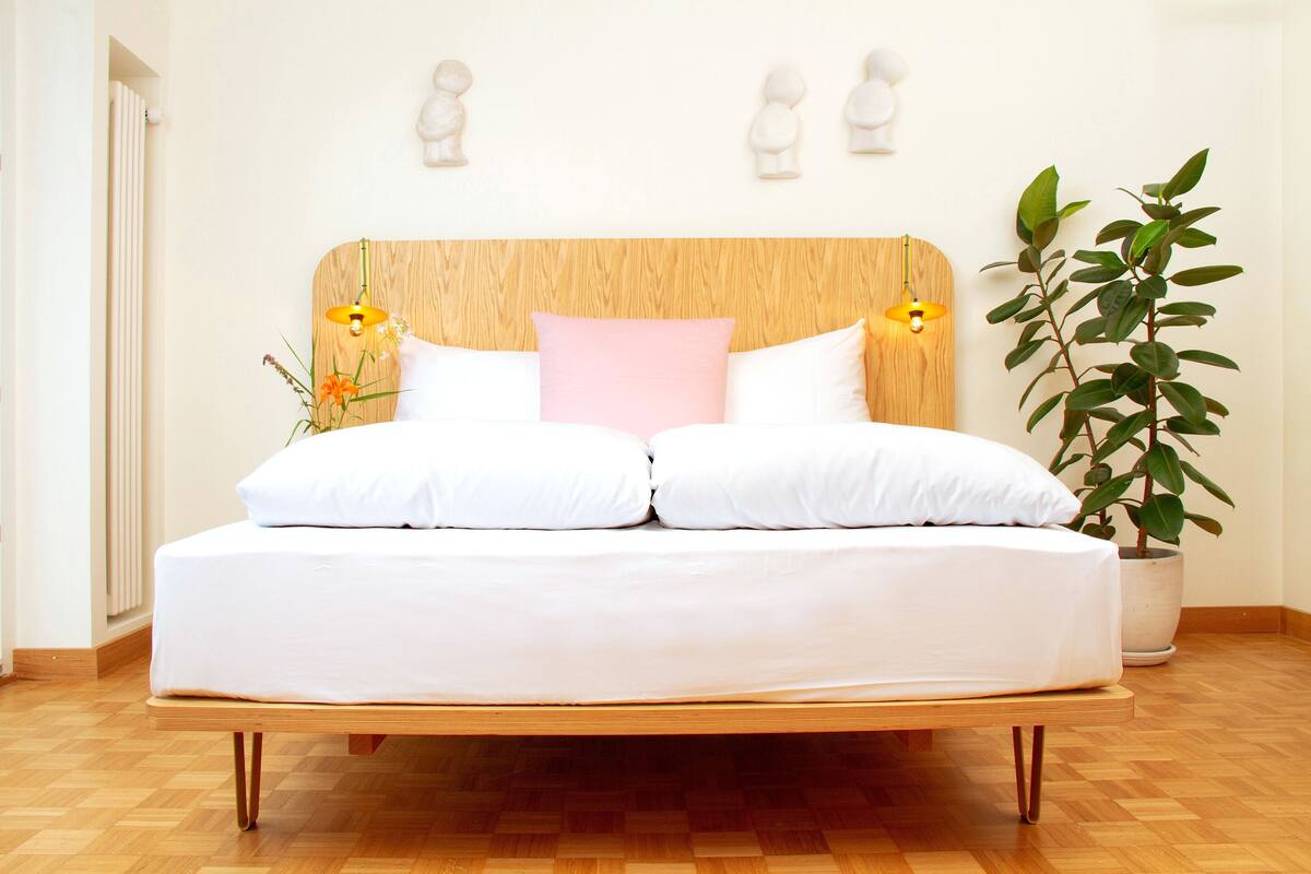 Een bed met een houten hoofdbord, witte beddengoed en twee bedlampjes.