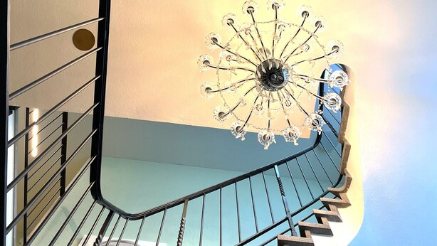 A spiral staircase with metal railings and a decorative crystal chandelier at the top. - Villa Maria (Lucerne)