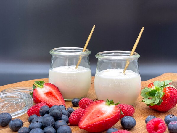 Dos frascos de vidrio con pajitas de madera, llenos de un líquido blanco, rodeados de fresas, frambuesas y arándanos sobre una superficie de madera.
