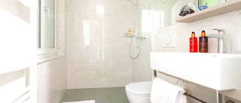 Une salle de bain moderne avec une douche à parois de verre, des toilettes blanches et un meuble-lavabo doté d’un miroir et d’une étagère.