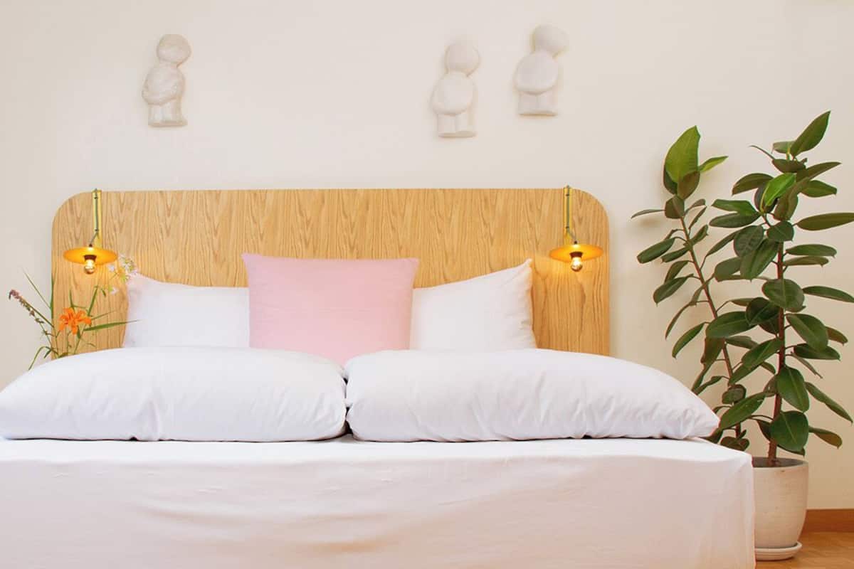 Een net opgemaakt bed met witte lakens, een houten hoofdbord en twee bedlampjes.