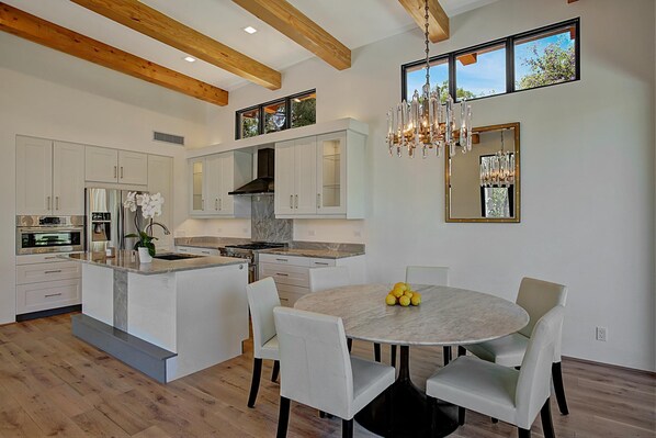A modern kitchen with white cabinetry, a central island, and a dining area with a marble table and chairs.