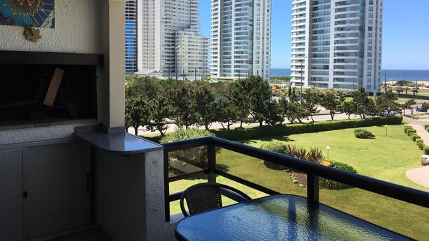 A balcony with a view of high-rise buildings and a grassy area.