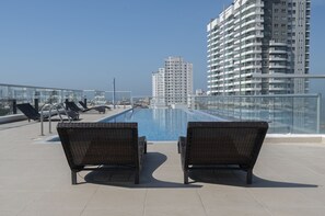 Ein Poolbereich auf dem Dach mit zwei Korbstühlen, die zum Pool ausgerichtet sind, umgeben von Hochhäusern.
