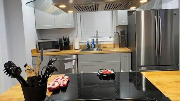 Een moderne keuken met een glazen kookplaat, roestvrijstalen apparatuur en een houten aanrecht.