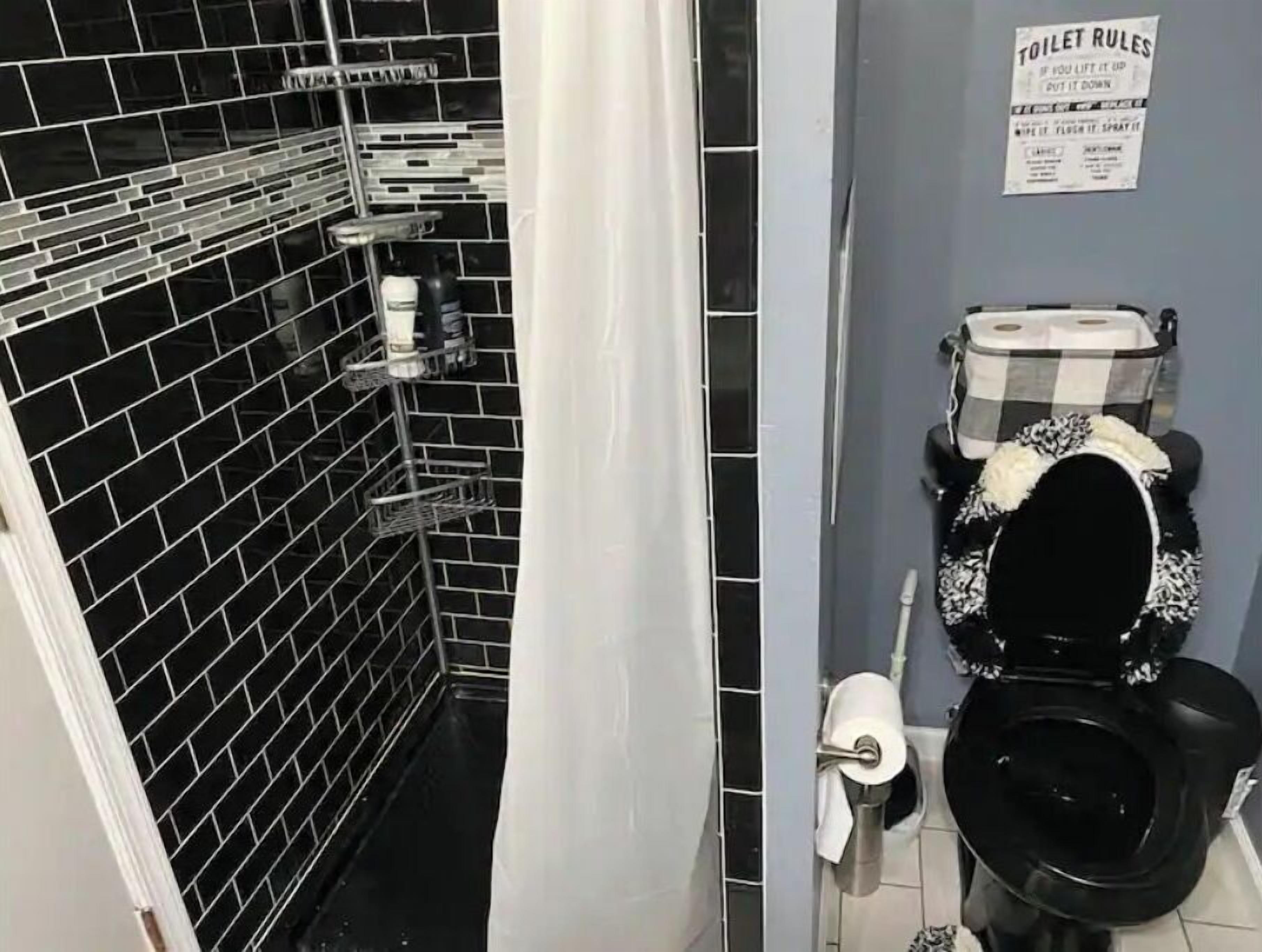 Ett badrum med svarta kakelväggar, en svart toalett och en vit duschdraperi. På väggen finns en skylt med regler för toalettanvändning.