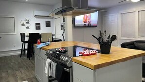 Een moderne keuken met een centraal eiland, een inbouwoven en een grote televisie aan de muur.