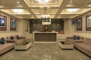 A modern lobby with a reception desk, two sofas, a chandelier, and framed artwork on the walls.