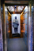 An elevator with a poster of a person, a ceiling with a geometric light pattern, and a marble wall.