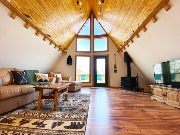 Un salon spacieux avec un haut plafond, une cheminée, un téléviseur et une grande fenêtre.