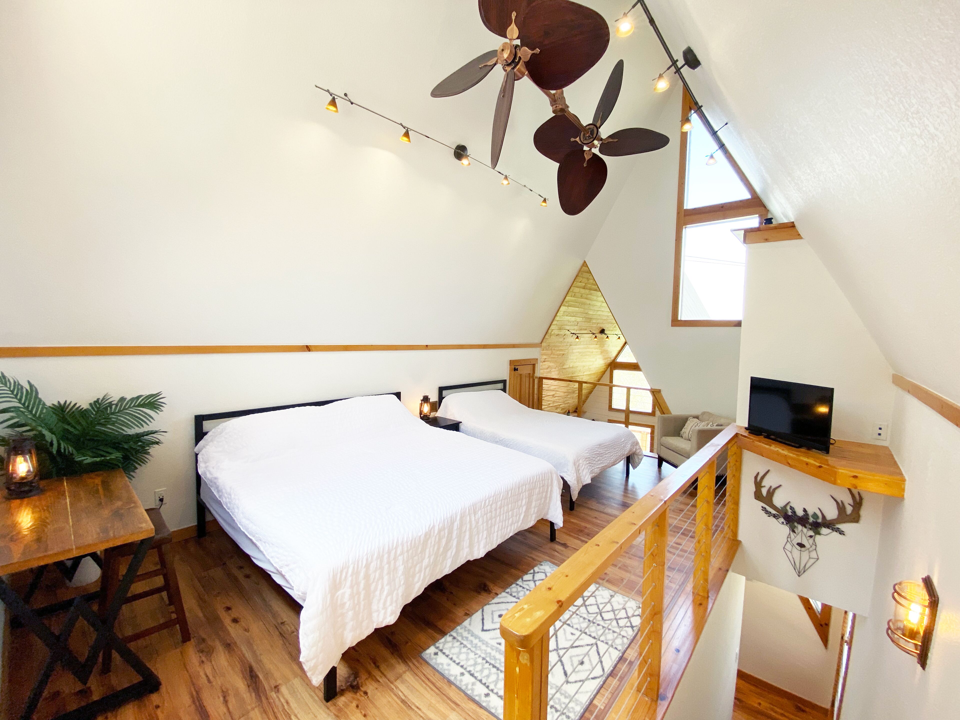Une chambre avec deux lits, un ventilateur de plafond, une télévision et un escalier en bois.