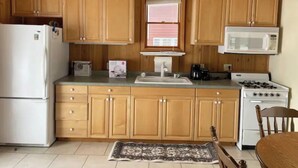 A compact kitchen with wooden cabinets, a refrigerator, a microwave, a stove, and a sink.