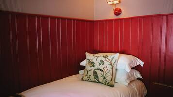 A room with a bed, a pillow with a bird design, and a wall-mounted lamp.
