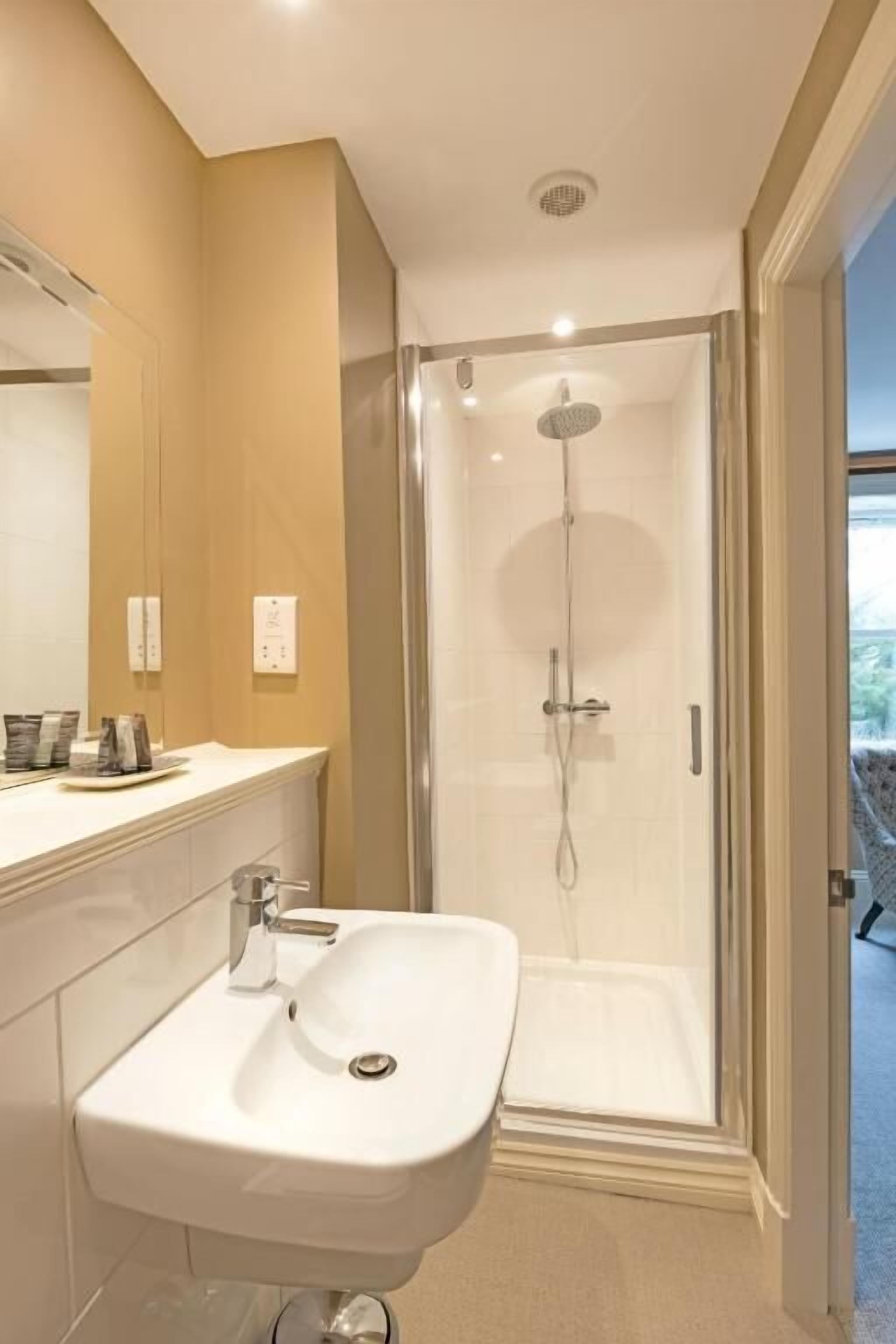 Une salle de bain moderne avec une douche à parois de verre, un lavabo blanc et un miroir au-dessus.