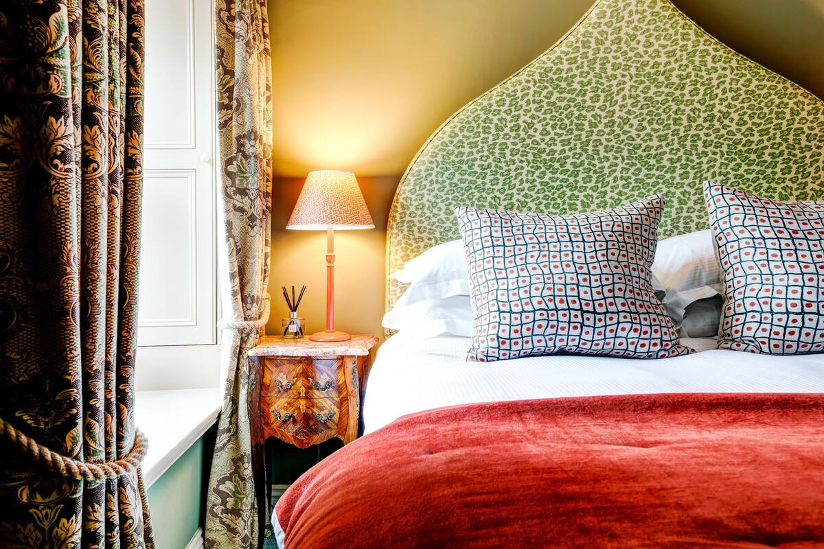A hotel room with a bed, patterned pillows, a bedside lamp, and curtains.