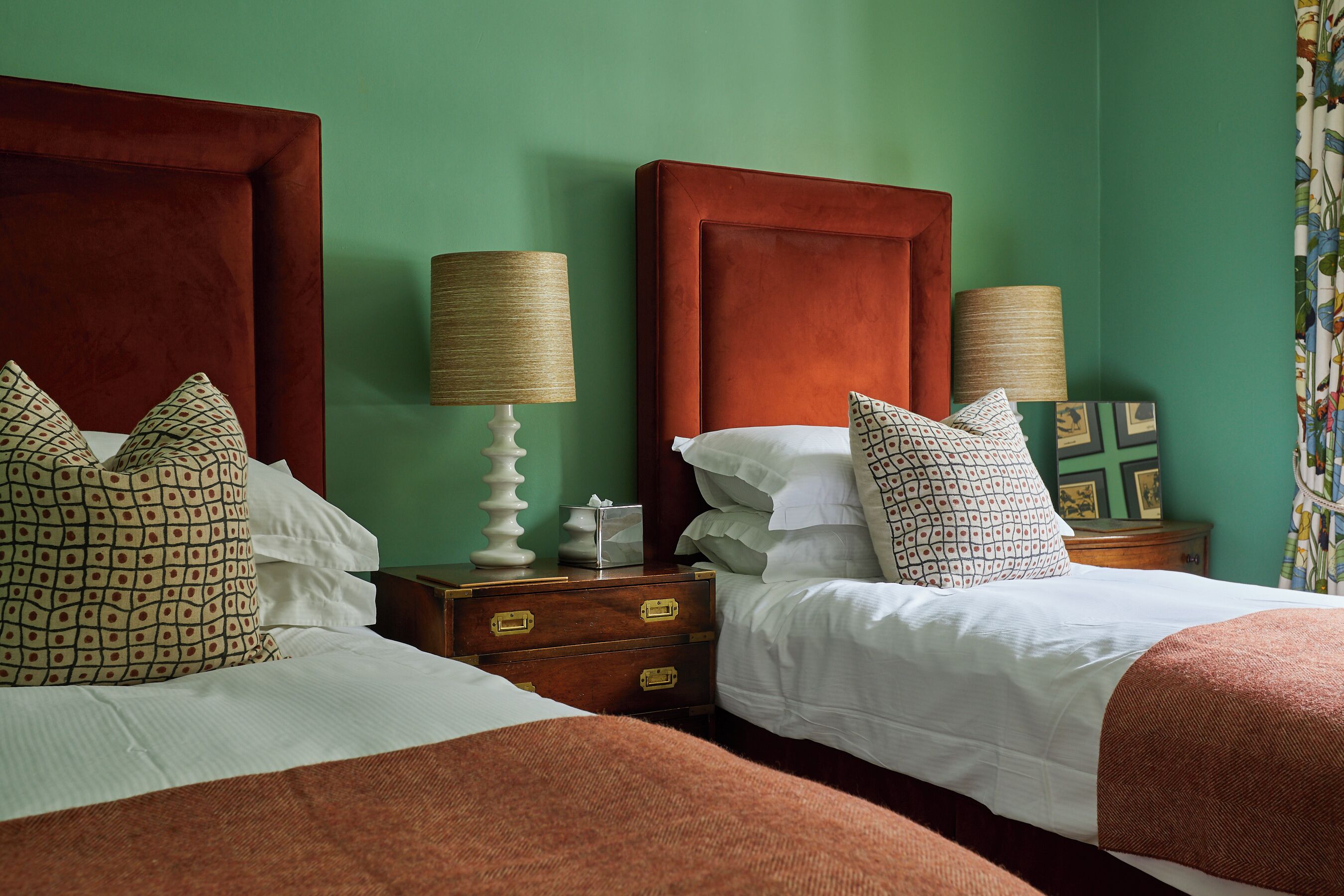 Una cama doble con cabecera de madera, dos mesitas de noche con lámparas y almohadas estampadas.