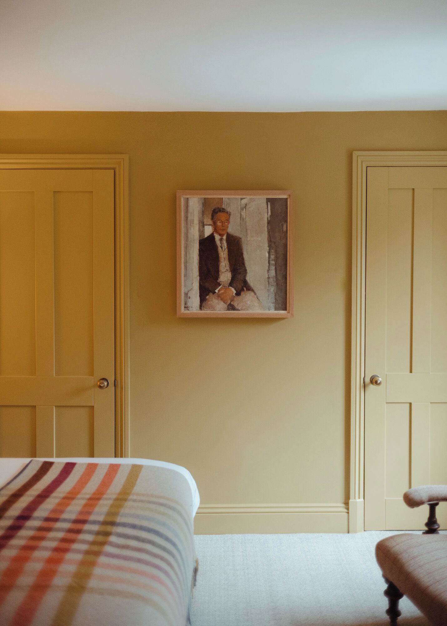 A hotel room with a bed, a painting on the wall, and two doors.