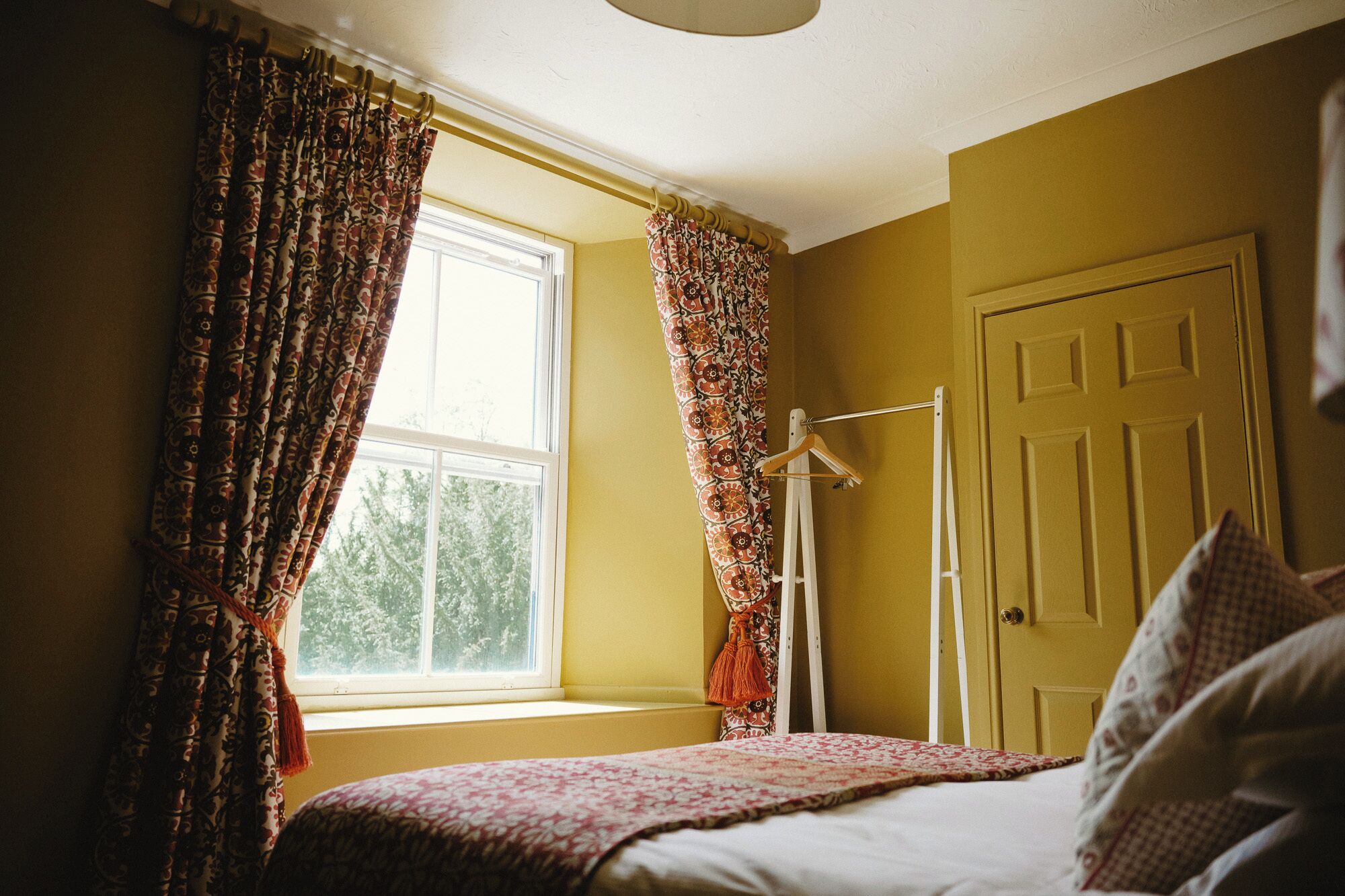 A bedroom with a bed, a window with curtains, a door, and a coat rack.
