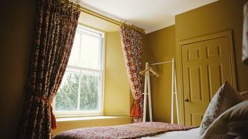 A bedroom with a bed, a window with curtains, a door, and a coat rack.