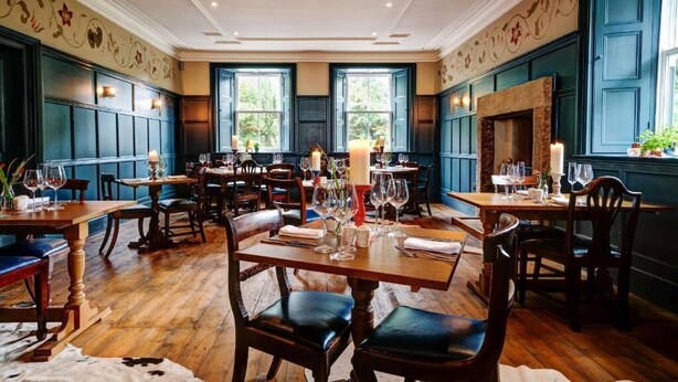 Un restaurante con mesas y sillas de madera, una chimenea y ventanas amplias.