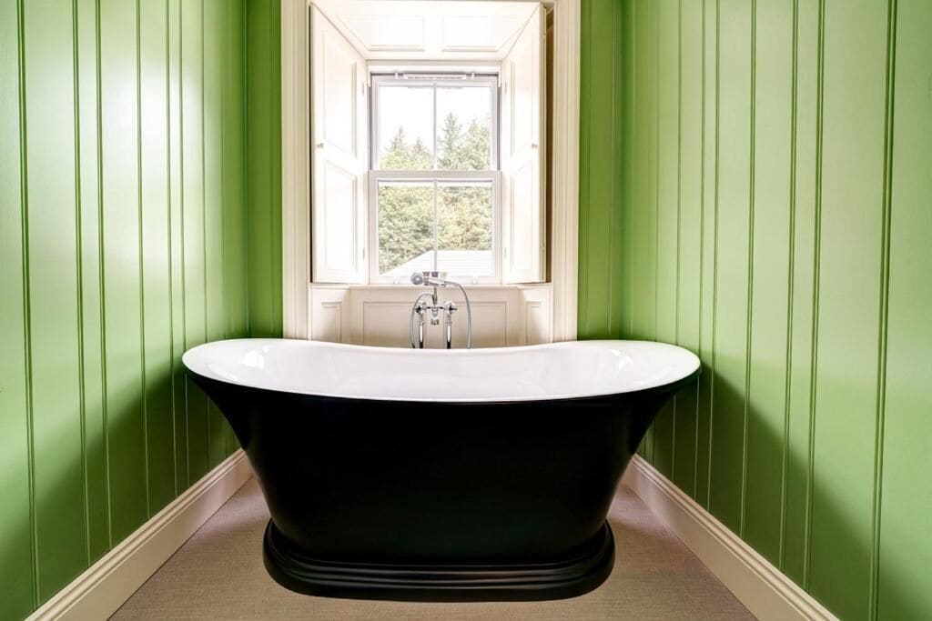 Eine freistehende Badewanne in einem Raum mit grünen Wänden und einem Fenster darüber.