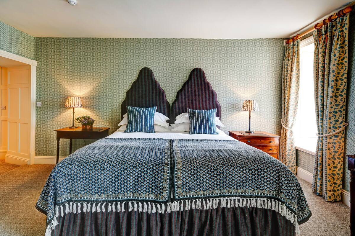 A bedroom with a large bed, two bedside tables, and a window with curtains.