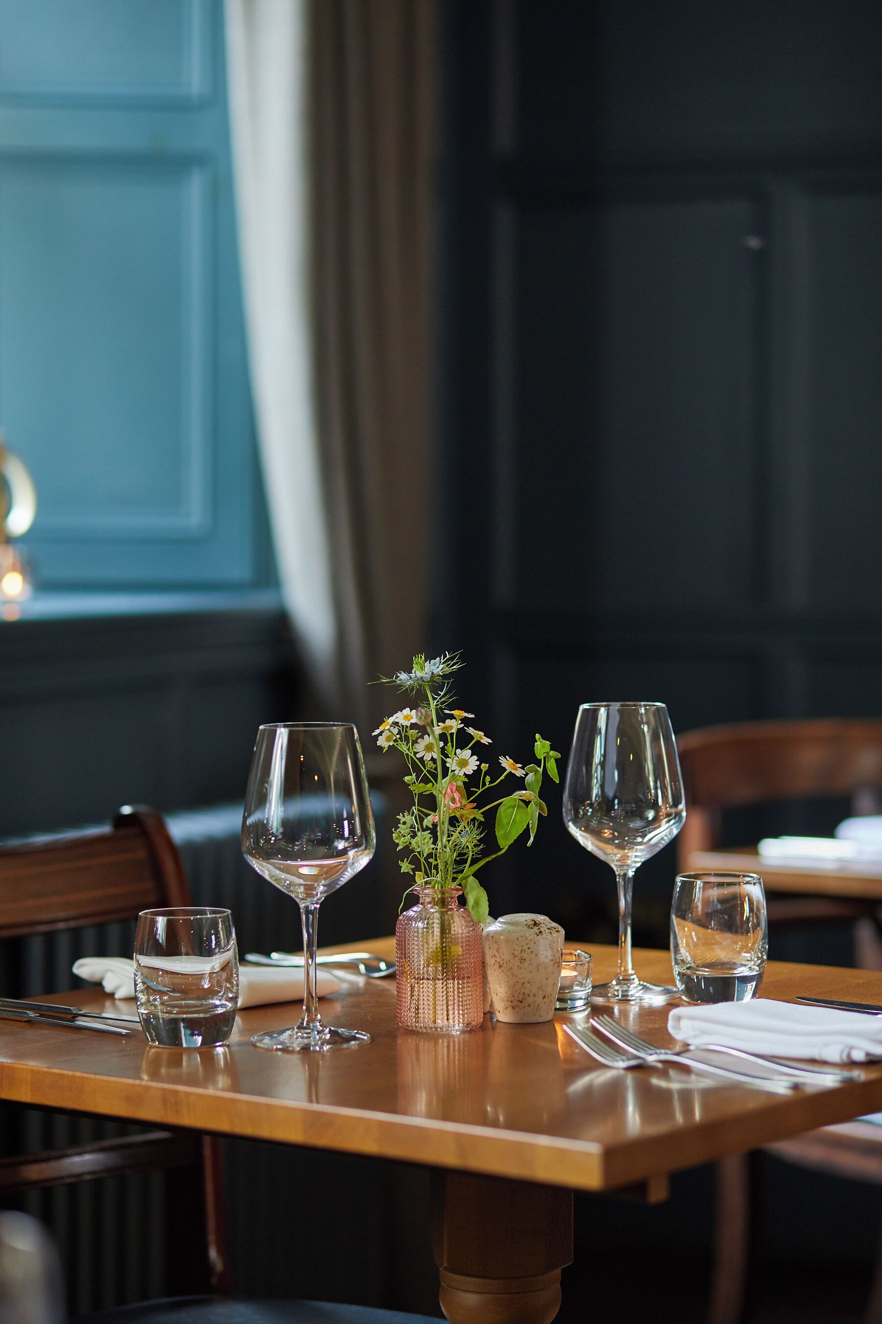 A dining table set with empty wine glasses, a small vase with flowers, and a candle.