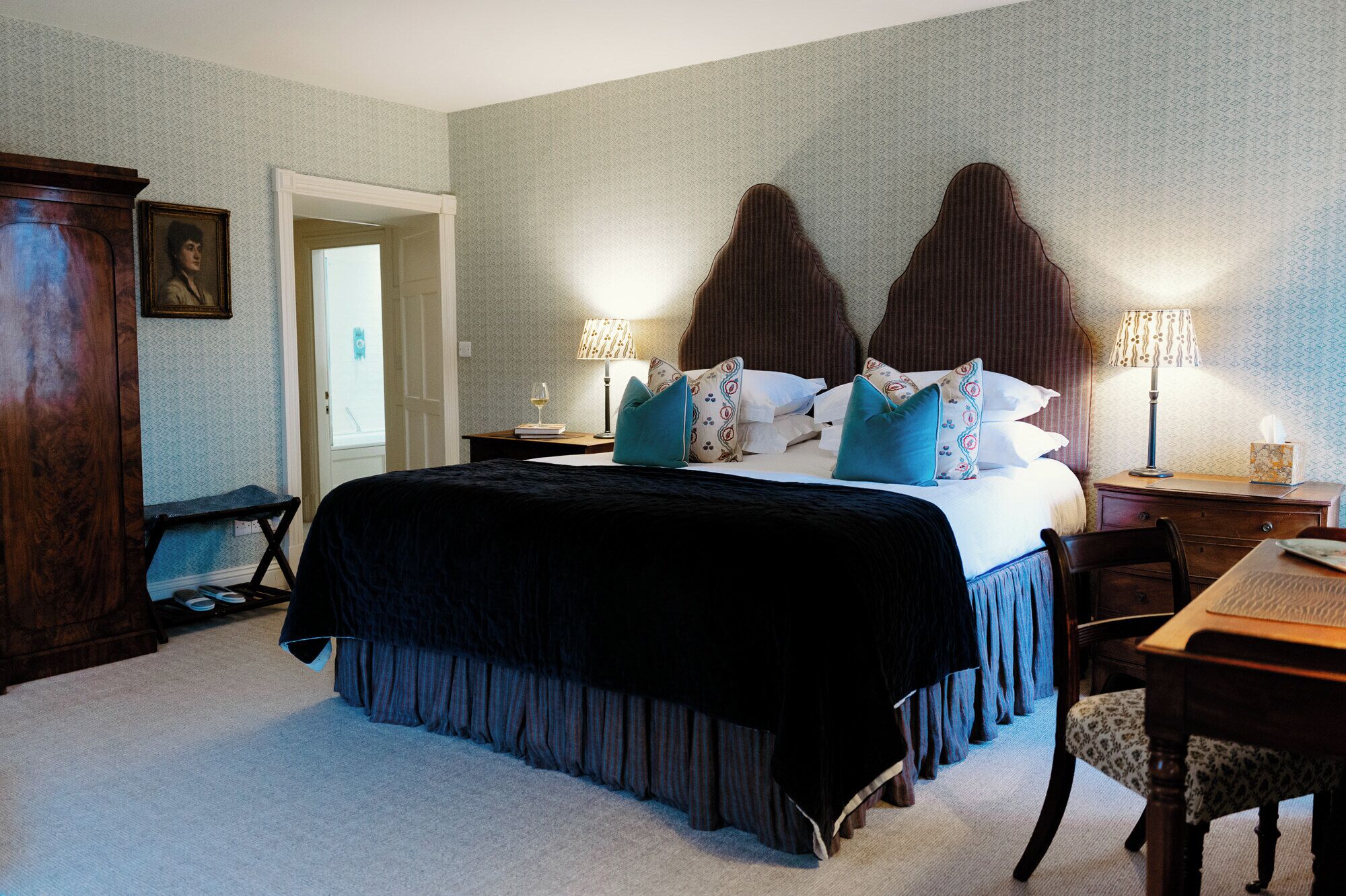 A hotel room with a large bed, two bedside lamps, a wooden dresser, and a desk with a chair.