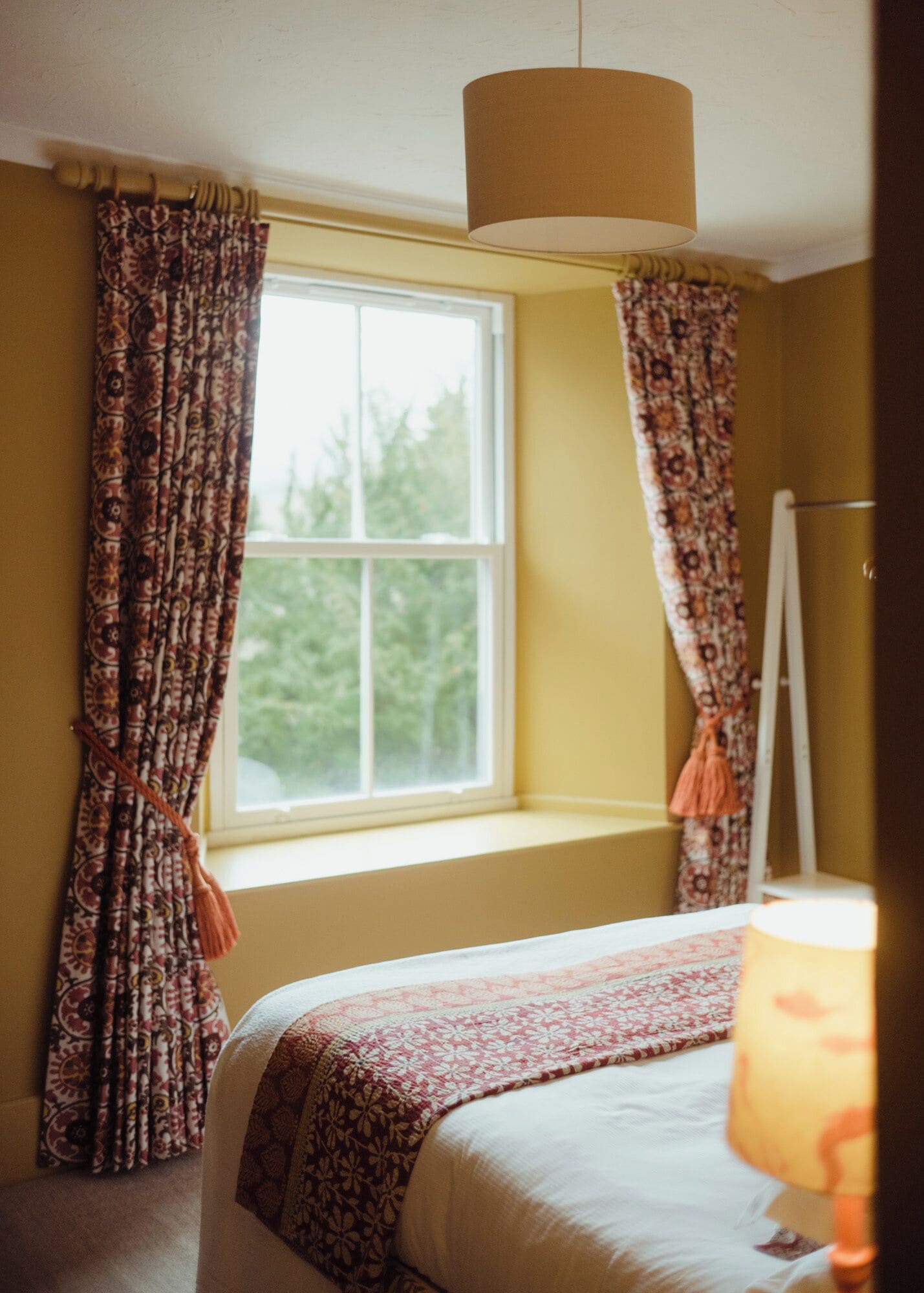 A room with a bed, a window with curtains, and a lamp.