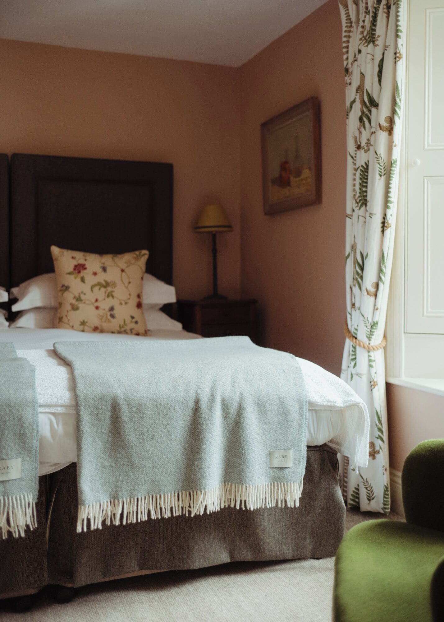A neatly made bed with a headboard, a bedside lamp, and a floral pillow.