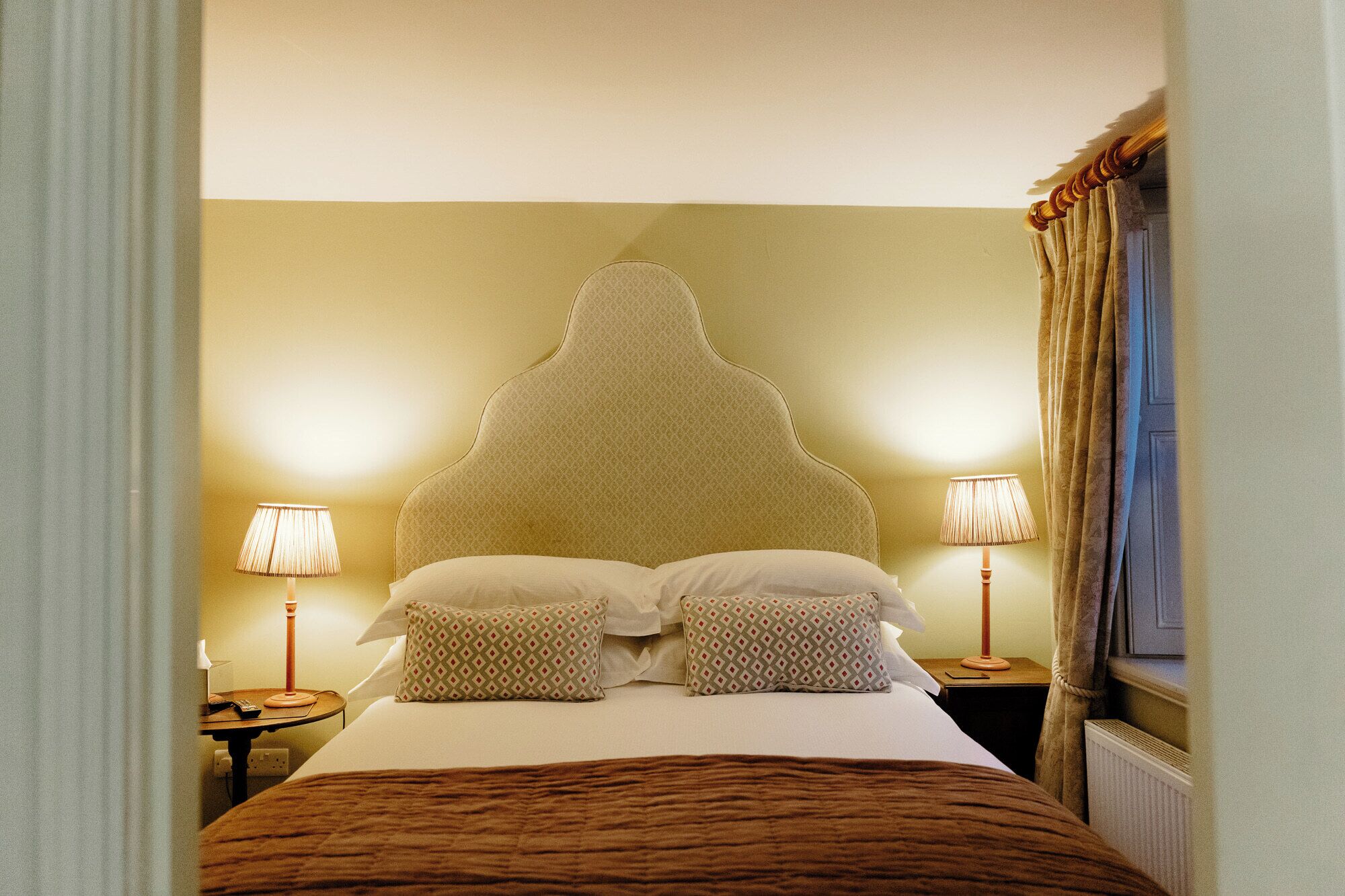 A hotel room with a large bed, two bedside lamps, and a window with curtains.