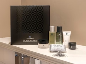 Een wastafelmeubel met een zwarte doos met de tekst 'Temple Spa' en diverse toiletartikelen, waaronder een fles, een potje en een buisje.