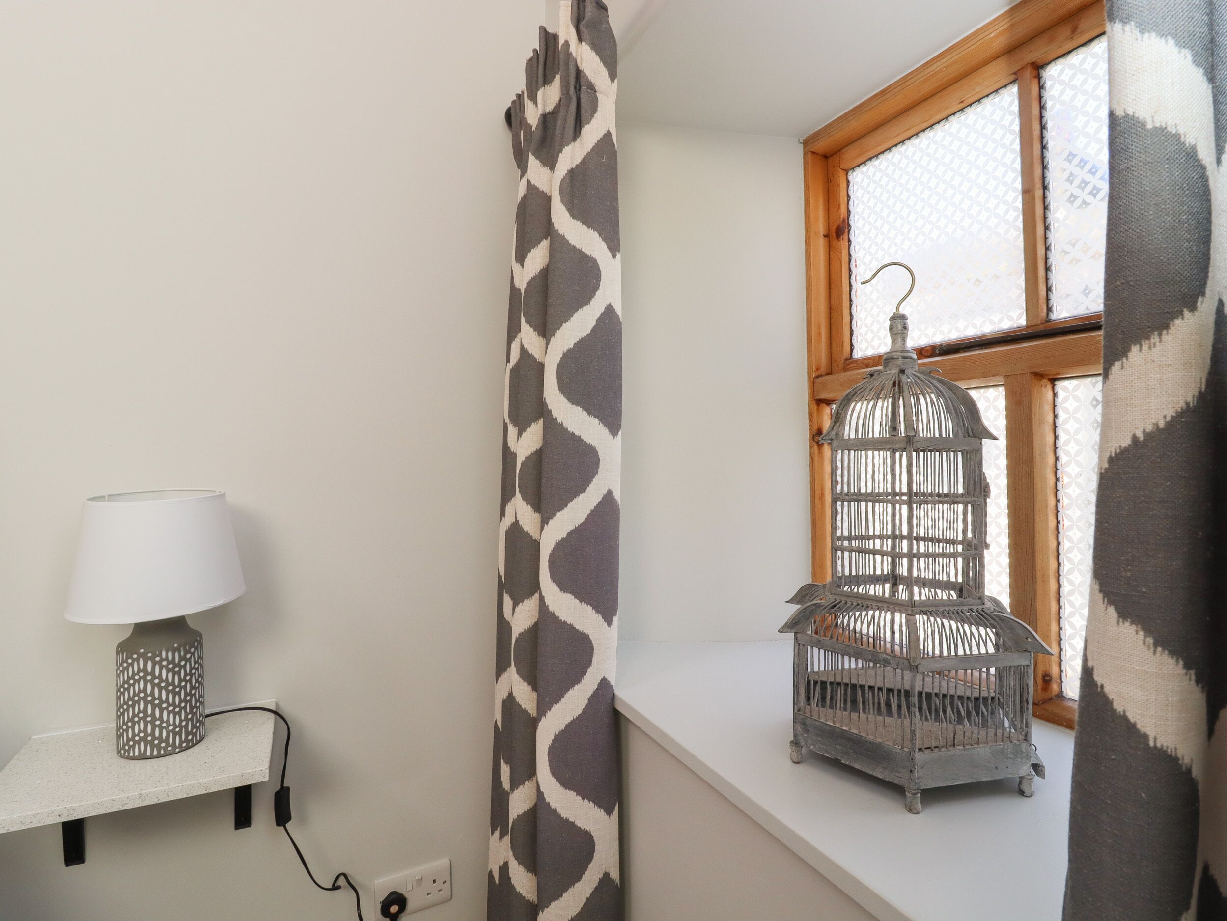 Een kamer met een raam, een lamp op een plank en een vogelkooi op de vensterbank.