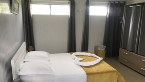 Habitació d'hotel amb un llit, una taula de nit amb una làmpada, un cistell de paper i un armari.