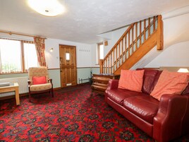 A living room with a red patterned carpet, a wooden staircase, a red leather sofa, and a wooden chair.