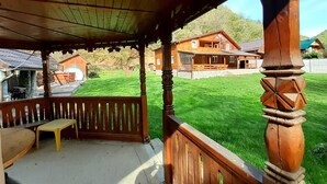 Un quiosco de madera con un banco, con vistas a un césped cuidado y casas de madera tradicionales.