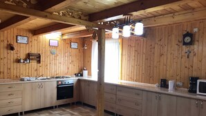 Una cocina con paneles de madera, que incluye una estufa a gas, horno y microondas. Hay armarios de madera, un lavamanos y una ventana con cortinas.