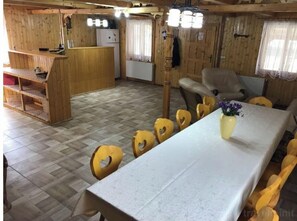 A wooden interior with a long dining table, heart-shaped chairs, a small kitchen area, and a wooden bench. - Valea Tonii B&B Strungari (Strungari)