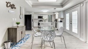 A modern kitchen with white cabinets, a central island, and a dining area with a glass table and metal chairs. - Reston NEW Bright, Airy Home w/ In Ground Pool & Grill (Richardson)