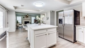 A modern kitchen with a central island, stainless steel appliances, and a dining area with a fireplace. - Reston NEW Bright, Airy Home w/ In Ground Pool & Grill (Richardson)